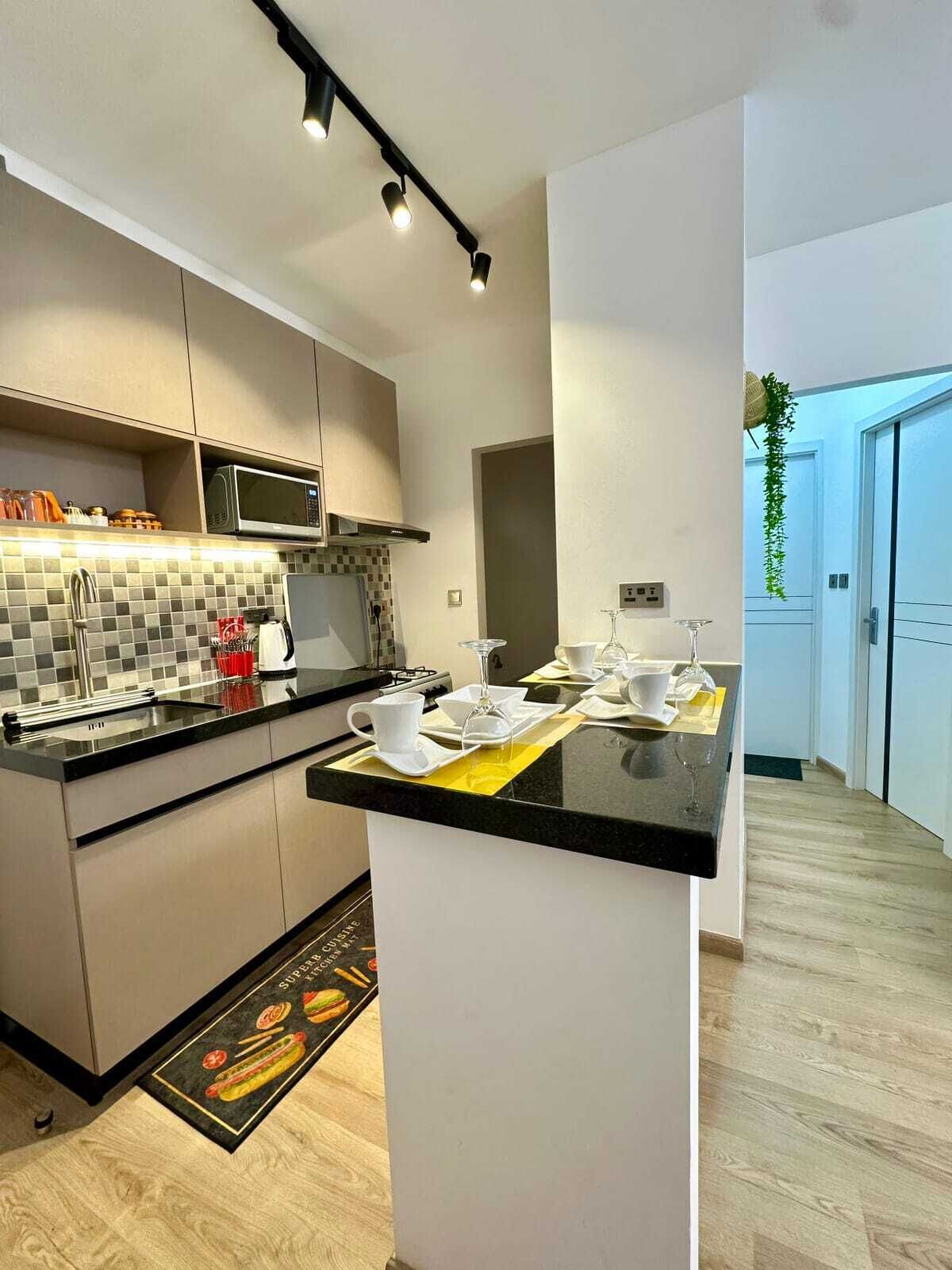 Uma cozinha moderna com ilha central, micro-ondas embutido e luminária pendente.