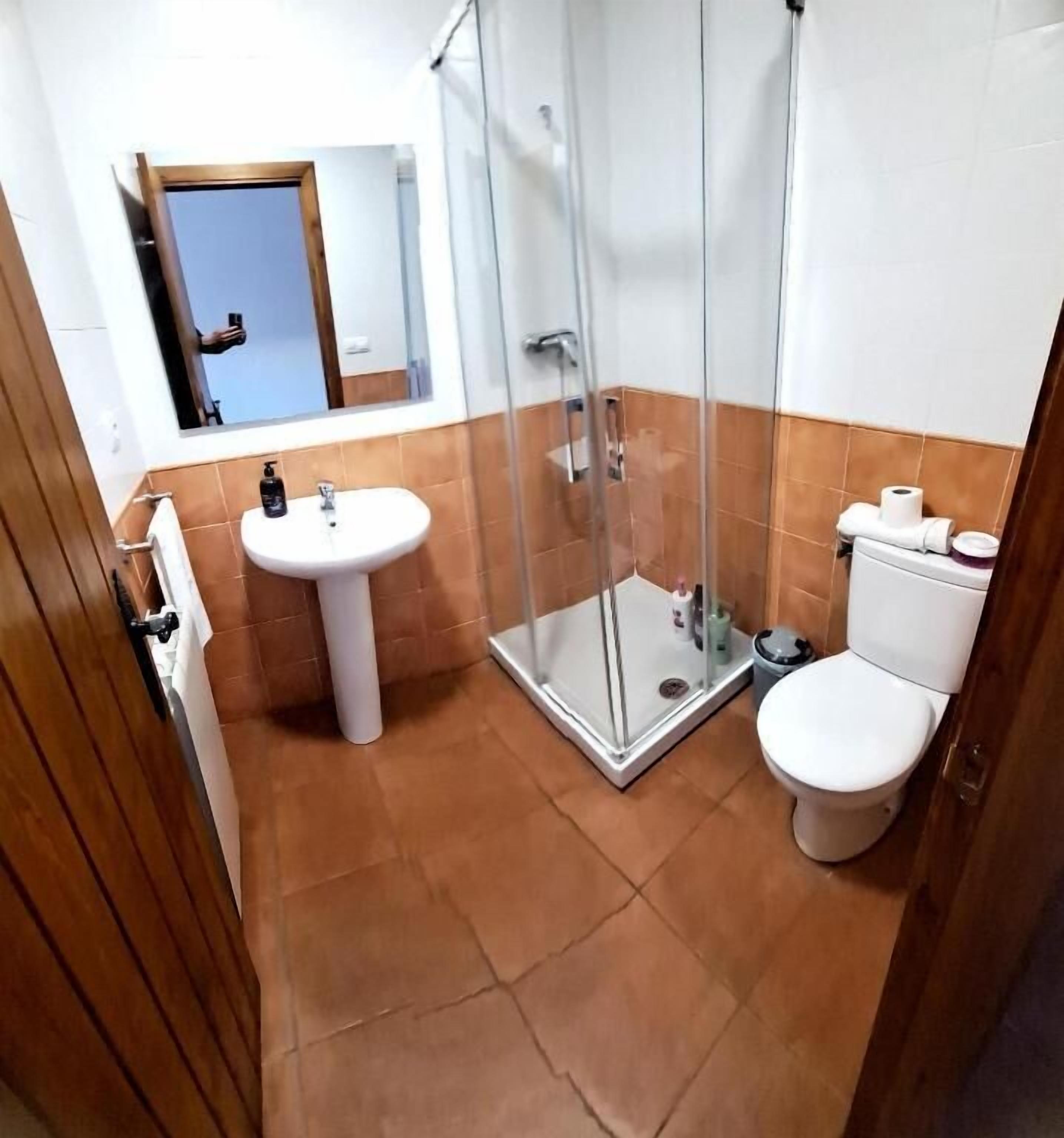 A bathroom with a glass shower enclosure, a pedestal sink, and a toilet.