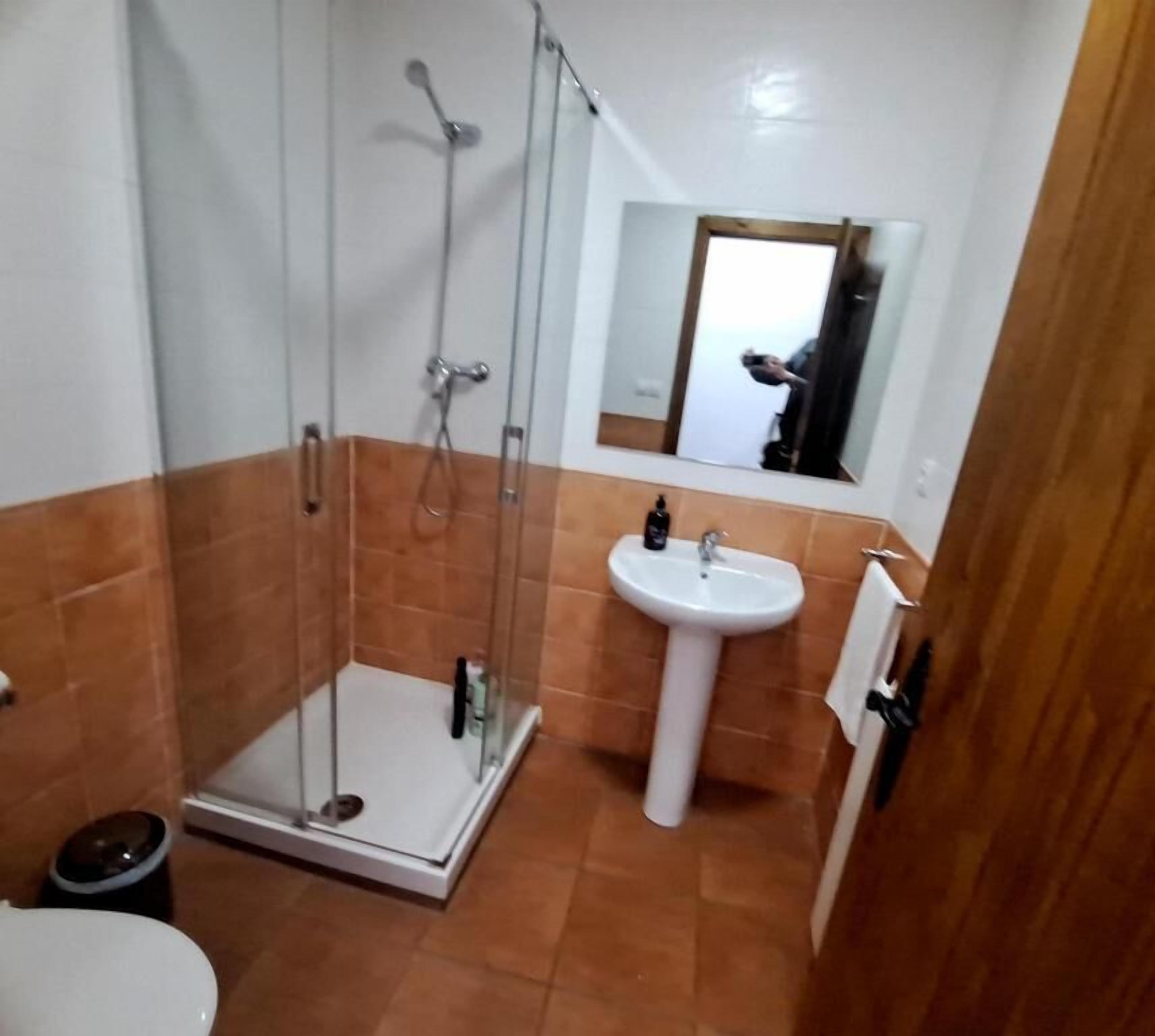 Une salle de bain avec une douche à parois de verre, un lavabo sur colonne et un miroir au-dessus du lavabo.
