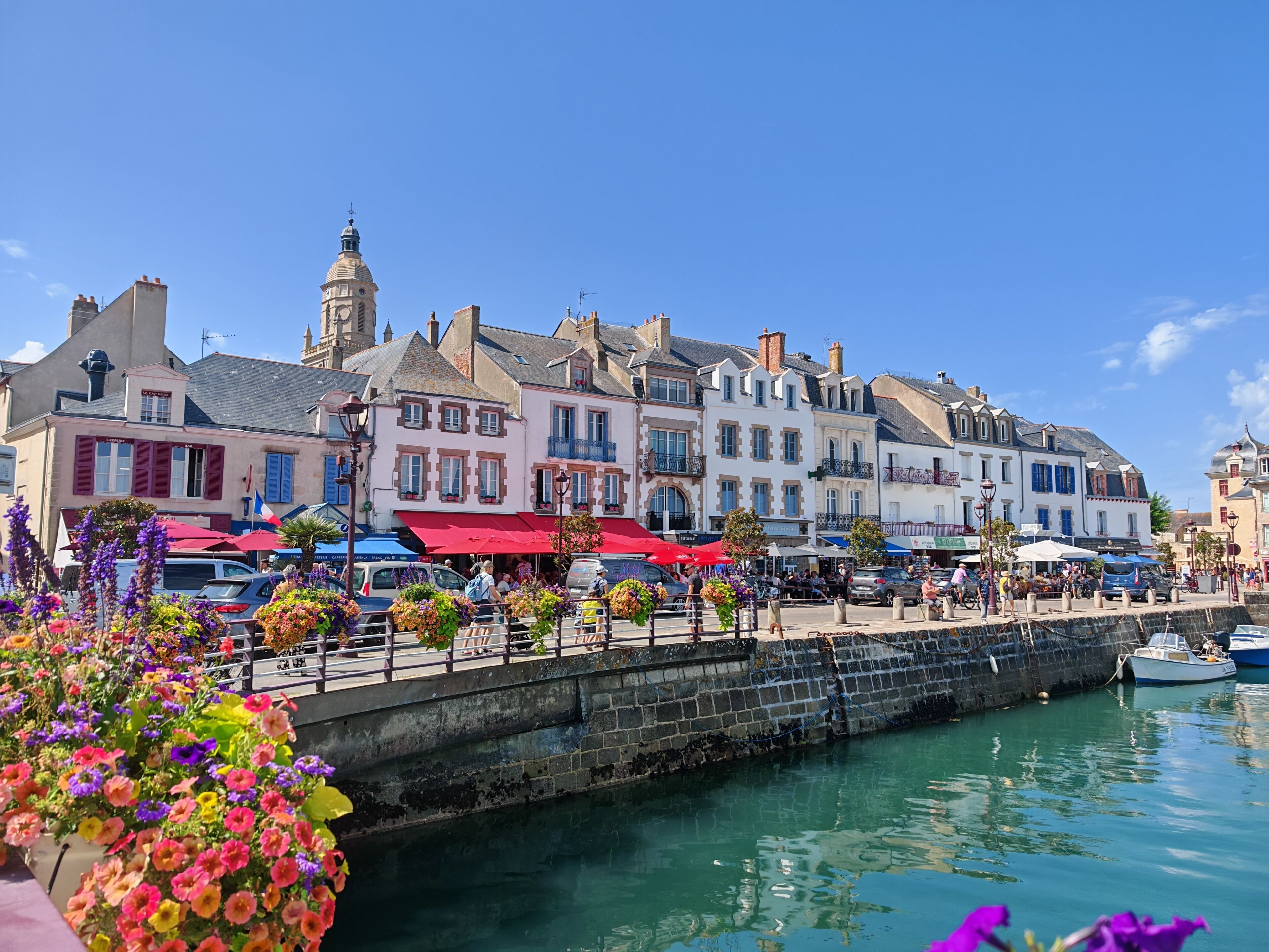 Une promenade en bord de mer, bordée de bâtiments historiques, d’un mur de pierre et donnant sur une étendue d’eau calme.