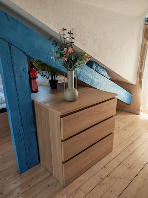 A wooden dresser with drawers, a vase with flowers, a red fire extinguisher, and a potted plant. - The Blue Anchor, a beautiful apartment near the harbor (Le Croisic)