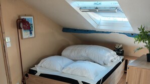 Un dormitorio con techo inclinado, tragaluz, cama de madera, mesita de noche y una pequeña planta en maceta.