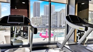 A gym with treadmills and a view of a cityscape through large windows. - 1BR, Marina & Bay View, High Floor, Resort (Hallandale Beach)