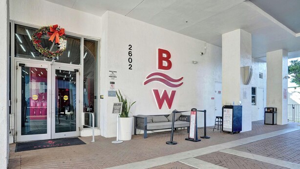 A hotel entrance with a glass door, a red and white logo, and a number '2602' on the wall. - 1BR, Marina & Bay View, High Floor, Resort (Hallandale Beach)
