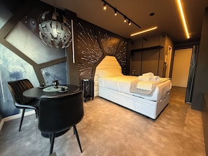 A modern bedroom with a bed, a dining table, and chairs, a decorative wall, and a ceiling light fixture. - Studio apartment - the comfortable side of the force (São Paulo)