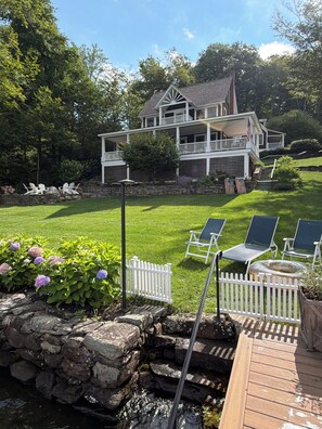 A two-story house with a front porch, a stone retaining wall, and a wooden deck with chairs. - DIRECT LAKEFRONT Property on Winsted Lake (Winchester)
