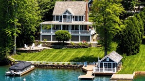 Una casa frente al lago con muelle, un bote y césped cuidado.