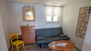 Una habitación pequeña y acogedora con un sofá, un aparador de madera, una silla amarilla y una mesa redonda de madera.