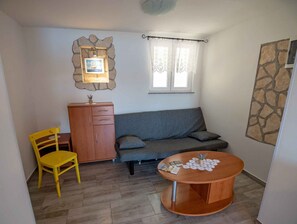 Una habitación pequeña y acogedora con un sofá, un aparador de madera, una silla amarilla y una mesa redonda de madera.