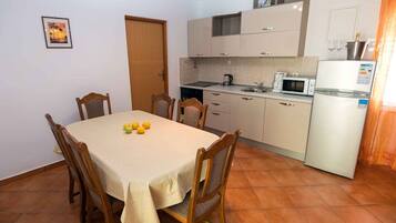 Comedor con una mesa dispuesta para cuatro personas, cocina con electrodomésticos básicos y una puerta que da a otra habitación.