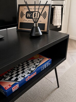 A black TV stand with a framed sign, a black desk lamp, and a chess board. - Lamani Homes | Cosy Nest Coventry | Stylish Studio Near City Centre ⭐ (Coventry)