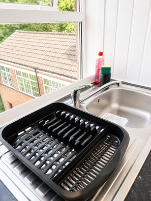 A kitchen with a stainless steel sink, a black grill pan, and a window overlooking a brick building. - Lamani Homes | Cosy Nest Coventry | Stylish Studio Near City Centre ⭐ (Coventry)
