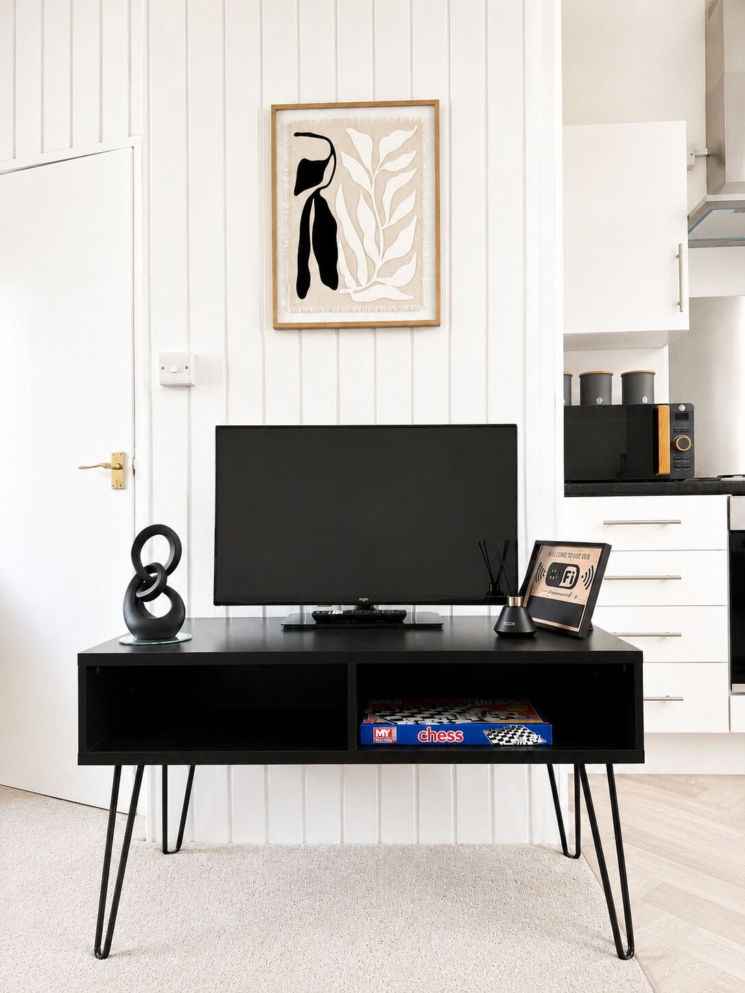A modern kitchen with a black TV stand, a framed artwork, and a chess set on the counter.