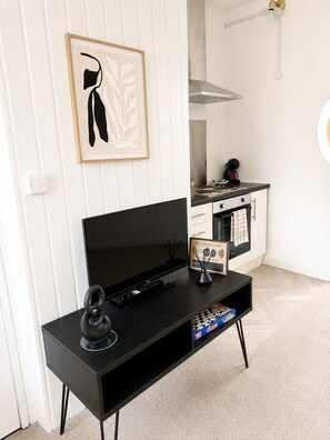 A modern living room with a flat-screen TV on a black stand, a small black table with a chess set, and a framed artwork on the wall. - Lamani Homes | Cosy Nest Coventry | Stylish Studio Near City Centre ⭐ (Coventry)