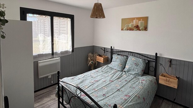 Ein Schlafzimmer mit einem Bett, einem Sessel, einem Fenster, einer Heizung und einer Pendelleuchte.