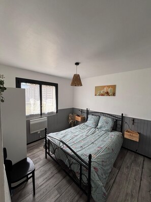 Ein Schlafzimmer mit einem Bett, einem Sessel, einem Fenster, einer Heizung und einer Pendelleuchte.