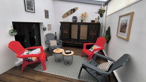 Ein gemütlicher Patio-Bereich mit zwei roten Stühlen, einem grauen Stuhl, einem kleinen runden Tisch und einer Vitrine mit Dekoration.
