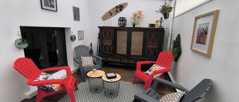 A cozy patio area with two red chairs, a grey chair, a small round table, and a cabinet with decorative items.