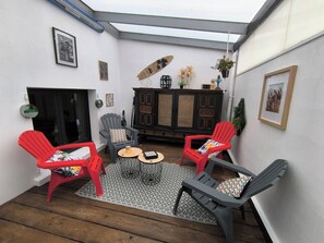 A cozy patio area with two red chairs, a grey chair, a small round table, and a cabinet with decorative items. - Small, quiet vacation home (Bretignolles-sur-Mer)