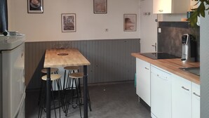 Eine kleine Küche mit Holztisch und Barhocker, weißen Schränken und einem Kühlschrank.