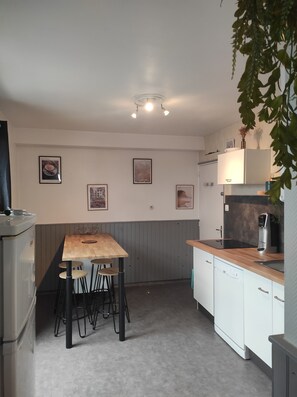 A compact kitchen with a wooden table and bar stools, white cabinets, and a refrigerator. - Small, quiet vacation home (Bretignolles-sur-Mer)