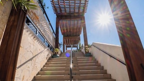 Una scala conduce a un'area coperta con una pergola, circondata da muri in pietra e piante in vaso.