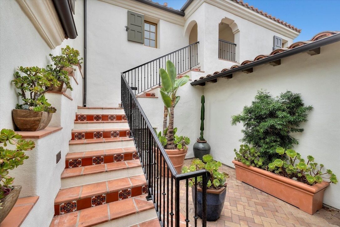 A staircase with red and brown tiles, flanked by potted plants and a black railing.