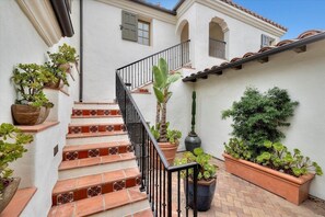 A staircase with red and brown tiles, flanked by potted plants and a black railing.