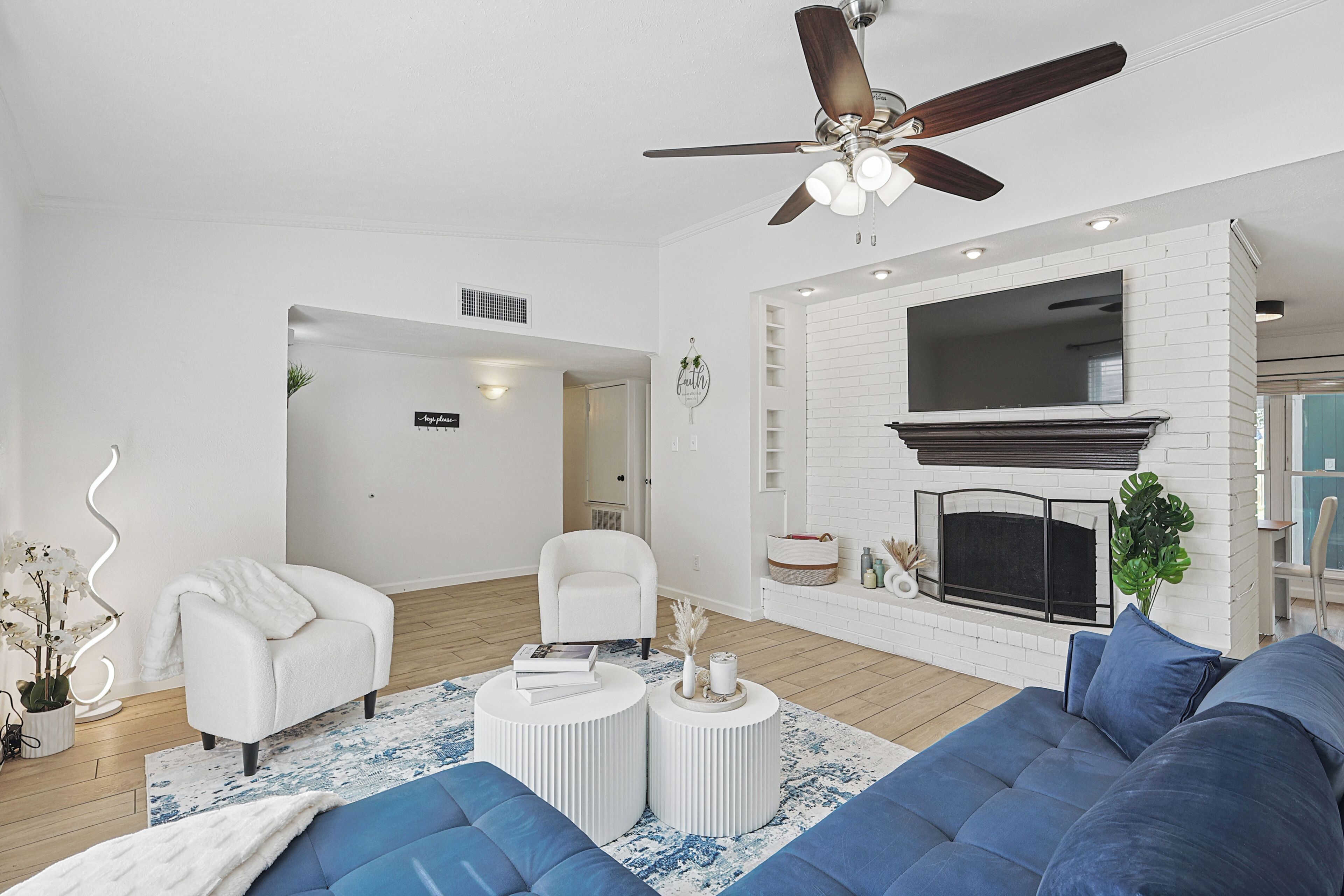 Un salon moderne avec un canapé blanc, un canapé bleu, un fauteuil blanc, un ventilateur de plafond et une cheminée.