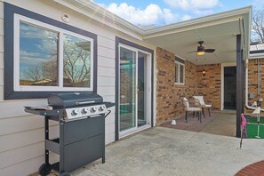 Ein Außenbereich mit Terrasse, einem Grill, einem Deckenventilator und einer Ziegelwand.
