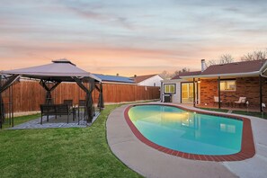 Ein Garten mit Swimmingpool, überdachter Terrasse und einem Ziegelhaus.