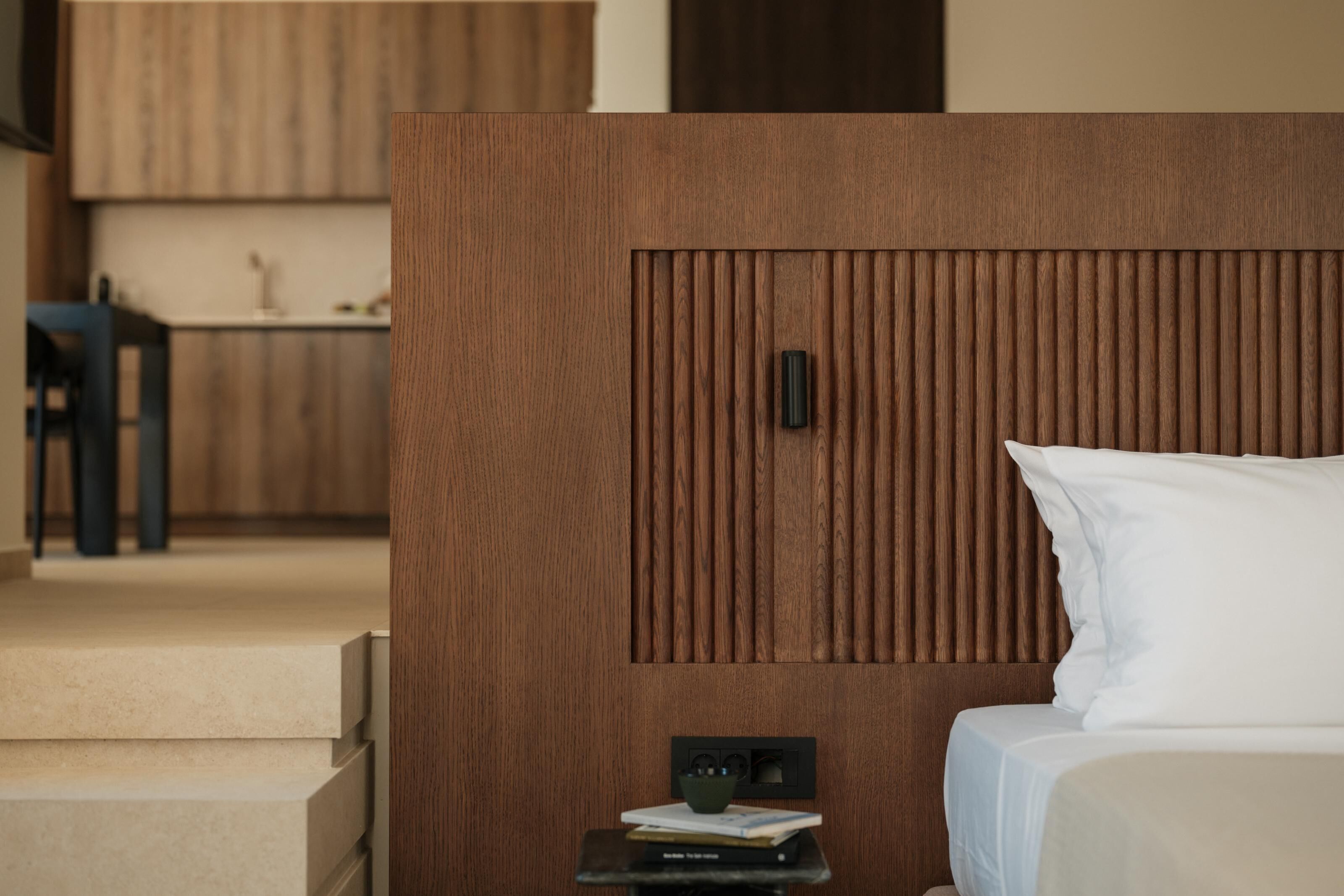 Una camera d'albergo con una testiera in legno, un comodino con una lampada e un letto con biancheria bianca.