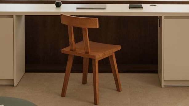Habitació moderna i minimalista amb una cadira de fusta, un escriptori i una planta.