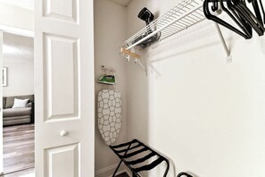 Une pièce avec une porte blanche, une planche à repasser fixée au mur, un portant à vêtements et une chaise.