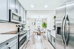 A modern kitchen with stainless steel appliances, a dining area with a round table and chairs, and a view of the outside.