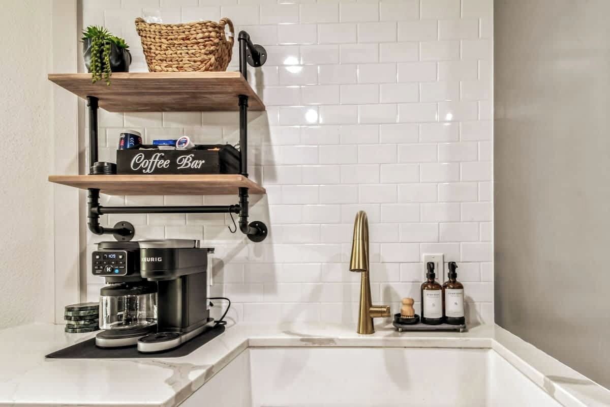 Une cuisine équipée d’une machine à café, d’étagères aménagées en coin café et d’un évier avec des bouteilles.