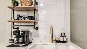 Une cuisine équipée d’une machine à café, d’étagères aménagées en coin café et d’un évier avec des bouteilles.