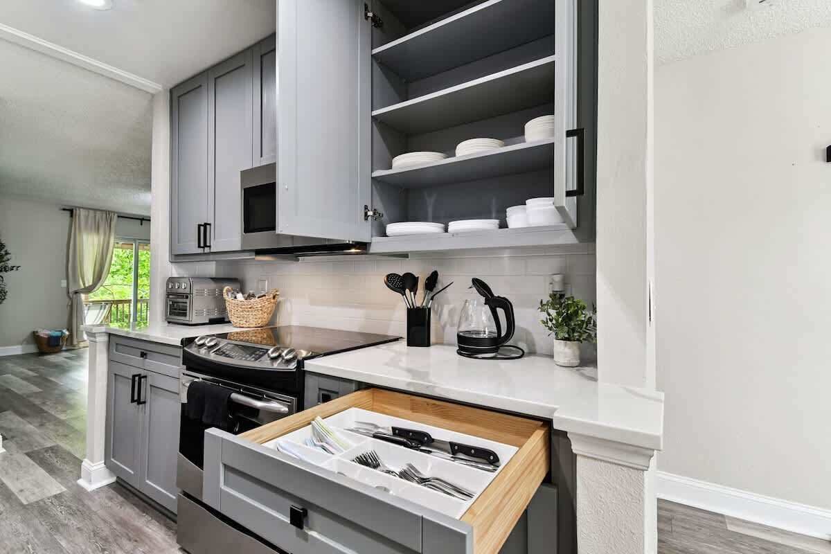 A modern kitchen with grey cabinets, a built-in oven, and a countertop with a coffee maker and utensils.