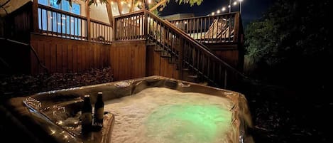 Un jacuzzi con cubierta de madera y luces colgantes, rodeado de árboles.