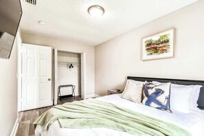 A hotel room with a bed, a nightstand, a bedside table, a door, and a framed picture on the wall.
