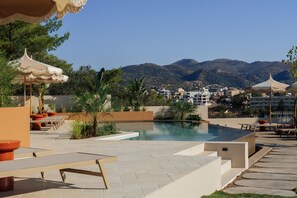 A pool area with lounge chairs and umbrellas, surrounded by greenery and overlooking a mountainous landscape. - Linum Hill Luxury 2BR Apt Ensuite Baths & Pool (Agios Nikolaos)