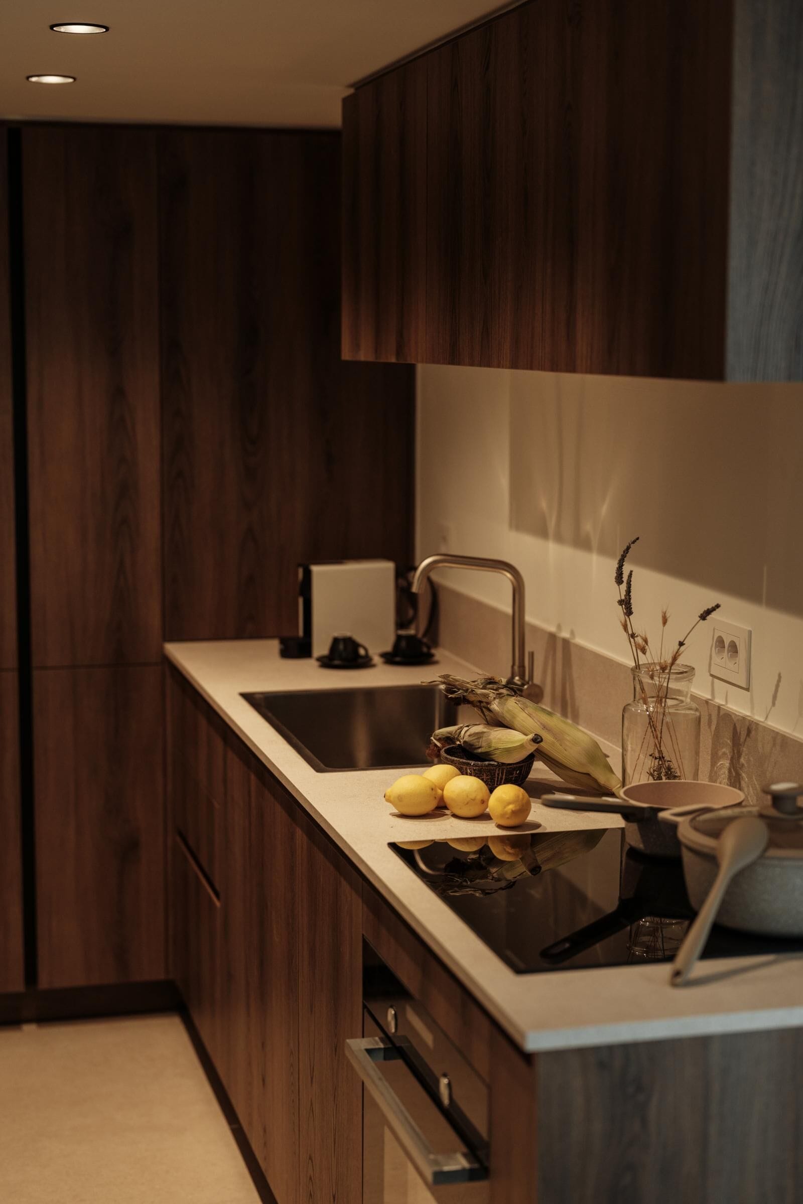 A modern kitchen with wooden cabinets, a stainless steel sink, and a countertop with lemons and corn.