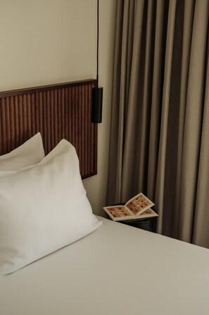 A hotel room with a bed, pillows, a nightstand with a book, and a wall-mounted light. - Linum Hill Luxury 2BR Apt Ensuite Baths & Pool (Agios Nikolaos)