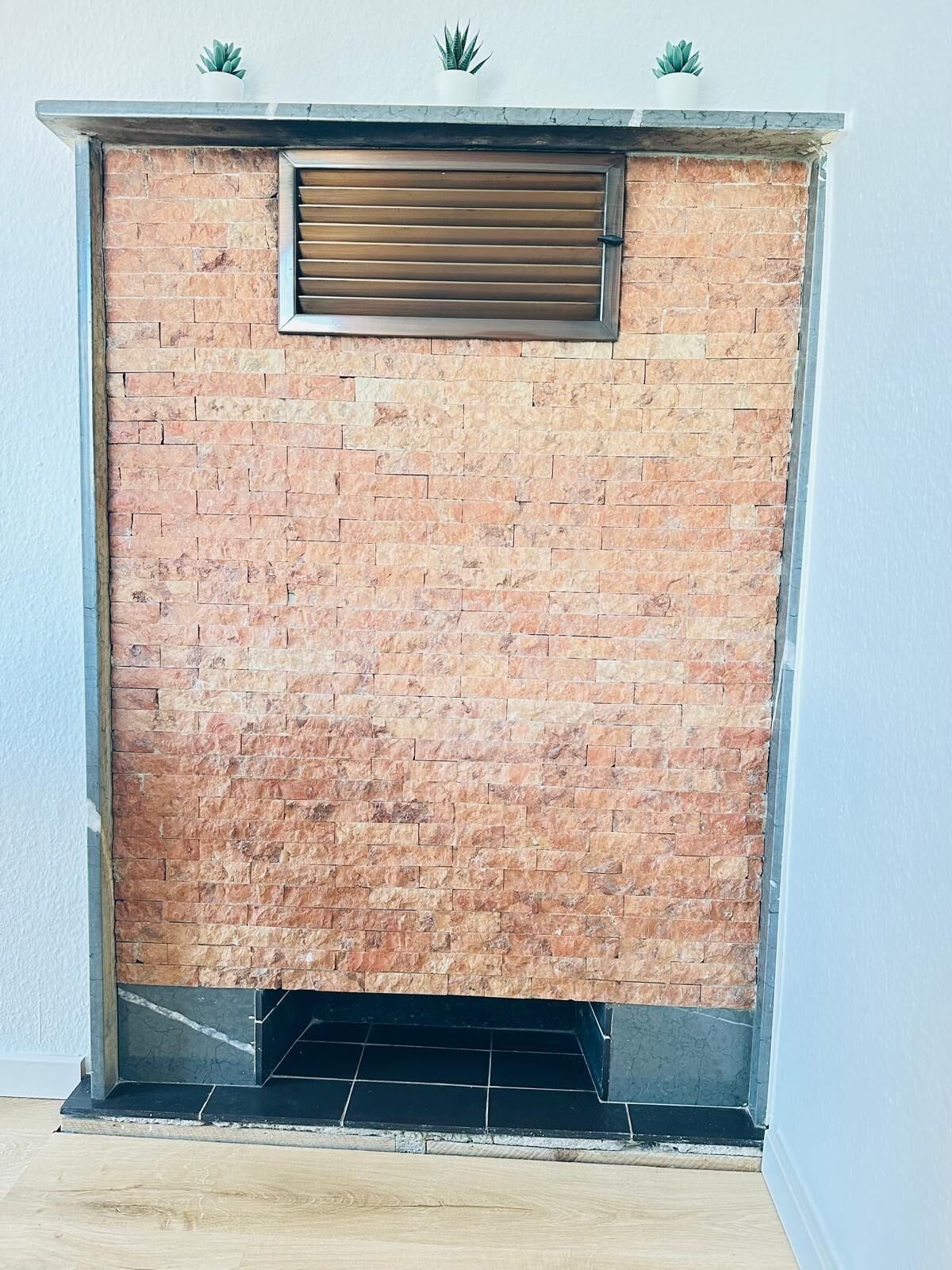 Ein Kamin mit Backsteinwand, Metallgitter und Fliesenfußboden.
