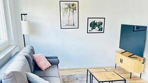 A modern living room with a grey sofa, a coffee table, a TV on a wooden stand, and two framed pictures on the wall. - Stylish apartment with a sun terrace (Heilbronn)