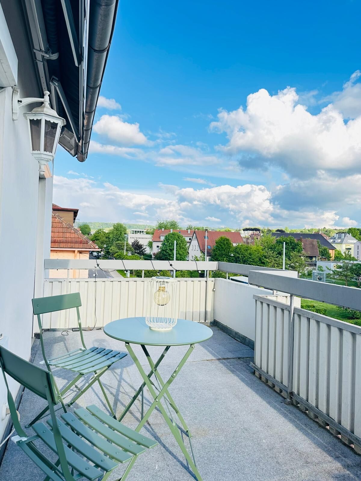 Un balcon avec une table et des chaises, une balustrade blanche et une vue sur des maisons et des arbres en arrière-plan.