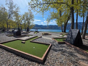 Un campo de mini golf con césped artificial verde, senderos de piedra y una vista panorámica de un lago.