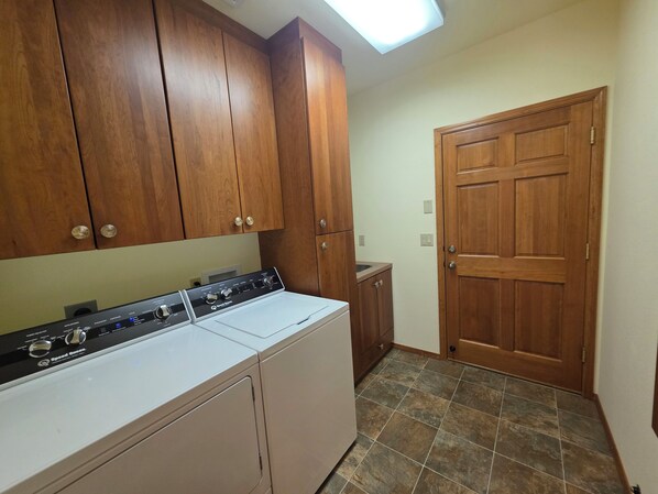 Un área de lavandería con lavadora y secadora, armarios de madera, piso de baldosas y una puerta de madera.