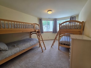 A bunk bed room with a ladder, a desk, and a window with curtains.