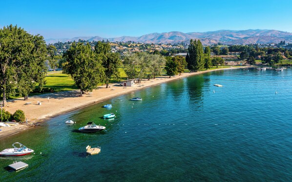 A lakeside view with boats, a sandy beach, and a park with trees.